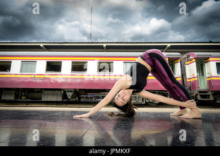 Flexibles Mädchen, das Yoga macht, posiert an einem Bahnhof, der Fitnesskleidung in Bangkok trägt Stockfoto