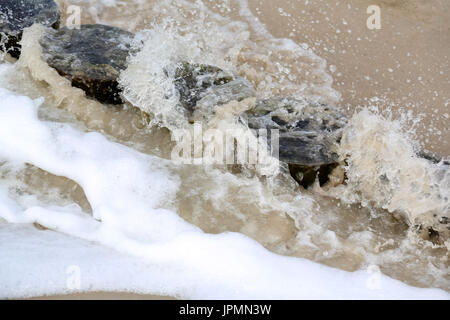 Das Meerwelle spritzte über die hölzernen Wellenbrecher. Es wird auf den sandigen Strand von Kolobrzeg in Polen gesehen. Stockfoto