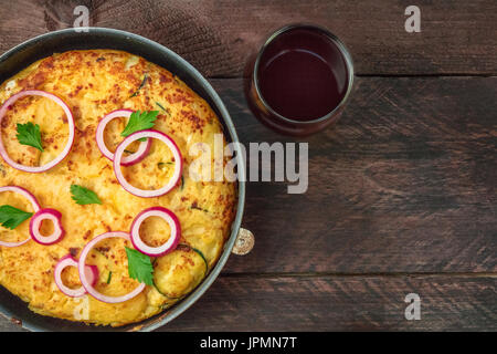 Eine obenliegende Foto eine spanische Tortilla mit Kartoffeln und Zucchini in eine Tortillera, mit einem Glas Rotwein und ein Platz für text Stockfoto