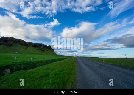Island - blauer Himmel über Straße zwischen grüner Wiese und Vulkangestein Stockfoto