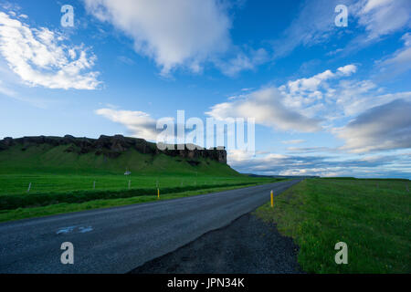 Island - blauer Himmel über Street zwischen der grünen Wiese und vulkanischen Gesteinen in der Morgendämmerung Stockfoto