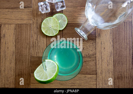 Vintage Gin gimlet cocktail in hohen Kugel aus Glas mit Scheiben von Kalk, Eiswürfeln und Glasflasche auf Holzbrettern. Stockfoto