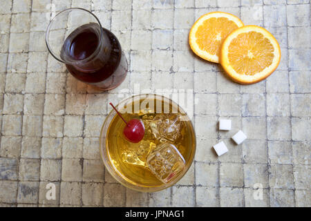 Klassische Old Fashion Bourbon cocktail auf Felsen garniert mit Cherry mit Würfelzucker, Orangenscheiben und Karaffe von Bourbon. Stockfoto