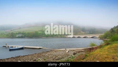 Panoramablick auf die Landschaft bei Ladybower Reservoir mit blauem Himmel und Nebel schwebt über Hügel am See mit angelegten Boot und Ashopton Viadukt in England Stockfoto