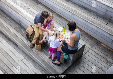 Junge Familie auf der High Line Park fördern ihre zwei jungen Mädchen, eine Take-Away Mittagessen gefüllte Pasta zu essen Stockfoto