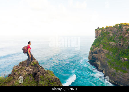 Mann Backpacker auf der Oberseite der Klippe Hügel genießen Landschaft Blick hindu Tempel Uluwatu Tempel in Bali Indonesien auf erstaunliche Natur Hintergrund Stockfoto