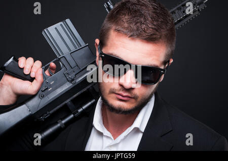 Closeup Portrait des männlichen Gangster mit automatischen Waffen auf dunklem Hintergrund in die Kamera schaut Stockfoto