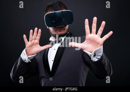 Angst oder überrascht eleganter junger Mann mit Vr-Brille erleben Vr Spiel auf dunklem Hintergrund isoliert Stockfoto