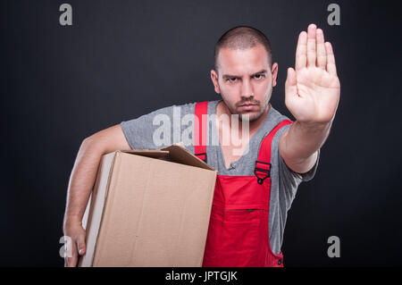 Ernsthafte Mover Mann hält Kasten zeigt Stop Geste auf schwarzem Hintergrund Stockfoto