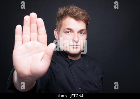 Schöner Kochen Koch zeigt Stop-Schild mit seiner Handfläche auf dunklem Hintergrund isoliert Stockfoto