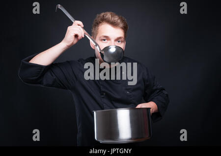 Männlichen Chef in einheitlichen Verkostung seiner frische Suppe von Ladel auf dunklen Studio-Hintergrund Stockfoto