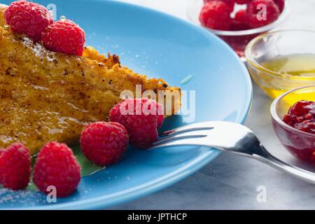 French Toast schließen Sie Mahl serviert auf blaue Platte mit Himbeeren und Schüsseln mit Honig und Marmelade Stockfoto