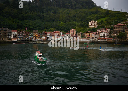 Boat Crossing service und ein trainera Training vor Fischerdorf Pasajes de San Juan (Pasai Donibane), bei Einbruch der Dunkelheit. Baskenland, Spanien. Stockfoto