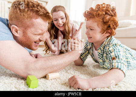 Seitenansicht von Vater und Sohn spielen Arm wrestling mit Mutter in der Nähe von zu Hause Familienspaß Konzept Stockfoto