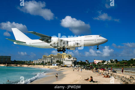 ein Verkehrsflugzeug Boeing 747 auf sehr niedrigen Finale-Ansatz über einen Strand mit Menschen und Hotels hinter Stockfoto