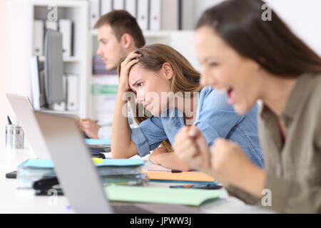 Frustrierte Mitarbeiter neben erfolgreichen einer Lesung Neuigkeiten auf Linie in einem Desktop im Büro sitzen Stockfoto