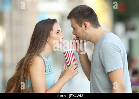 Seite Ansicht Porträt ein glückliches Paar teilen eine Take-away Erfrischung auf der Straße Stockfoto