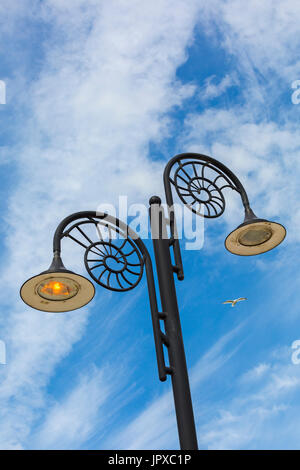 Reich verzierte Ammoniten Design Lampen spiegeln die Städte Lage an der Jurassic Coast, eine beleuchtete und eine nicht beleuchtet, auf Promenade bei Lyme Regis, Dorset Juli Stockfoto