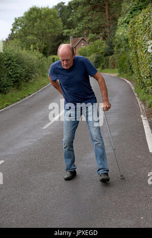 Ältere deaktiviert Mann mit Schmerzen im Rücken mit einem Gehstock Stockfoto