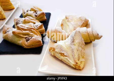 Gebackenes Gebäck, Brötchen bestreut mit Puderzucker auf langen Platten von Schwarz und weiß. Weiße Tischdecke Stockfoto