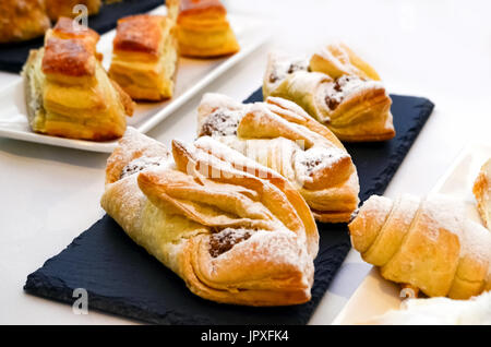 Ruddy Gebäck, Brötchen bestreut mit Puderzucker liegen auf langen Platten von schwarzer Farbe. Weiße Tischdecke Stockfoto