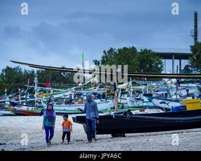 Kuta, Bali, Indonesien. 3. August 2017. Eine Familie geht es vorbei an Fischen Kanus am Jimbrana Strand in Kuta. Der Strand liegt in der Nähe des Flughafens und eine kurze Autofahrt von den anderen Stränden im Südosten Bali. Jimbrana war ursprünglich ein Fischerdorf mit einem geschäftigen Markt. Vor etwa 25 Jahren Entwickler begann mit dem Bau von Restaurants und Hotels entlang der Strand und Land Preise steigen. Der neue Schwerpunkt auf Tourismus verändert sich die Natur der Gegend, aber die Fischer sind noch damit beschäftigt, in den sehr frühen Morgenstunden. Bildnachweis: Jack Kurtz/ZUMA Draht/Alamy Live-Nachrichten Stockfoto
