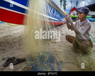 Kuta, Bali, Indonesien. 3. August 2017. Eine lokale Fischer repariert seine Netze neben seinem Auslegerboot am Jimbrana Strand in Kuta. Der Strand liegt in der Nähe des Flughafens und eine kurze Autofahrt von den anderen Stränden im Südosten Bali. Jimbrana war ursprünglich ein Fischerdorf mit einem geschäftigen Markt. Vor etwa 25 Jahren Entwickler begann mit dem Bau von Restaurants und Hotels entlang der Strand und Land Preise steigen. Der neue Schwerpunkt auf Tourismus verändert sich die Natur der Gegend, aber die Fischer sind noch damit beschäftigt, in den sehr frühen Morgenstunden. Bildnachweis: Jack Kurtz/ZUMA Draht/Alamy Live-Nachrichten Stockfoto