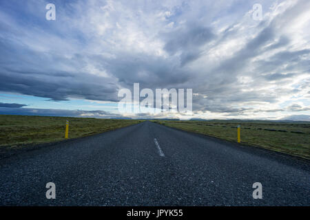 Island - kerzengerade Straße zwischen breiten grünen Land und Berge Stockfoto