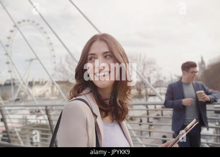 Lächelnde Frau zu Fuß auf städtische Brücke in der Nähe von Millennium Wheel, London, UK Stockfoto