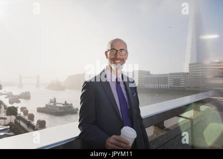 Porträt lächelnd, zuversichtlich Geschäftsmann Kaffeetrinken auf sonnigen städtische Brücke über die Themse, London, UK Stockfoto