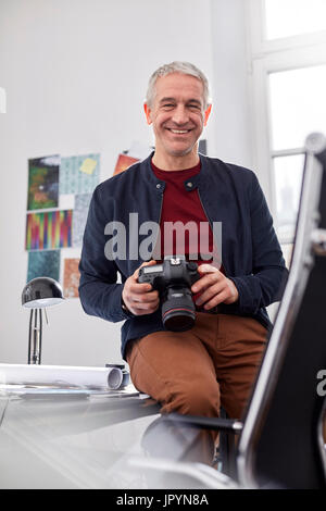 Lächelnd, selbstbewusste männliche Portraitfotograf mit Digitalkamera im Büro Stockfoto