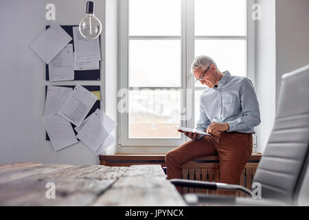 Geschäftsmann mit digital-Tablette in Bürofenster Stockfoto
