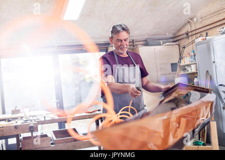 Männliche Zimmermann mit Luftkompressor, finishing Holz Kajak in Werkstatt Stockfoto