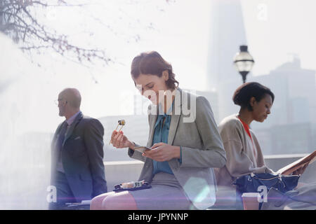 Geschäftsfrau auf Mittagspause Sushi-Essen und mit Handy im sonnigen Stadtpark Stockfoto