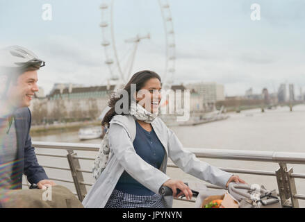 Lächelnd, unbeschwerte paar Fahrrad fahren auf die Brücke in der Nähe von Millennium Wheel, London, UK Stockfoto