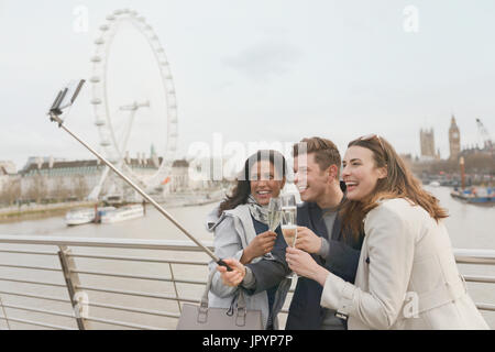 Lächelnd Freund Touristen feiern, toasten, Champagner und nehmen Selfie mit Selfie Stock in der Nähe von Millennium Wheel, London, UK Stockfoto