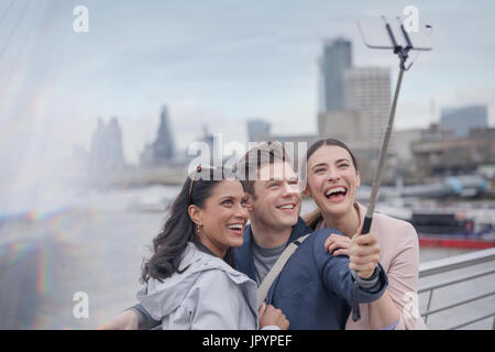 Enthusiastisch, lächelnd Freund Touristen nehmen Selfie mit Selfie Stick auf städtische Brücke, London, UK Stockfoto