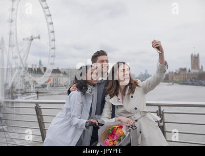 Lächelnd, glücklich Freunde nehmen Selfie mit Selfie Stick auf Brücke in der Nähe von Millennium Wheel, London, UK Stockfoto