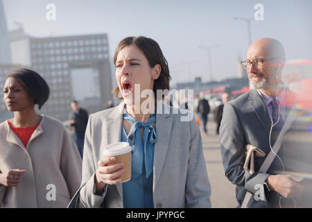Müde Geschäftsfrau mit Kaffee auf sonnigen Morgen urban Fußgängerbrücke Gähnen Stockfoto