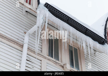Großen Eiszapfen hängen an der Fassade des hölzernen lebendigen Haus. Winter in Europa Stockfoto