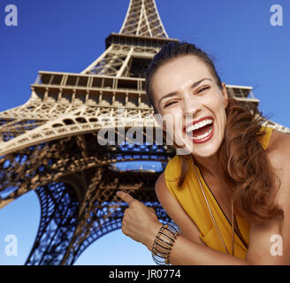 Touristisch, ohne Zweifel, aber noch nicht so viel Spaß gemacht. Porträt der glückliche junge Frau zeigte am Eiffelturm in Paris, Frankreich Stockfoto