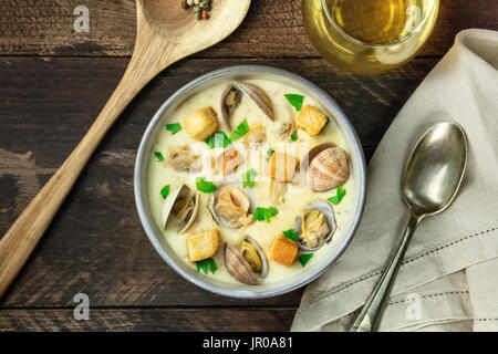 Eine obenliegende Foto aus einer Schüssel Muschelsuppe, dekoriert mit frischer Petersilie und Croutons, auf eine dunkle rustikale Textur mit einem Löffel, ein Glas Weißwein, Stockfoto