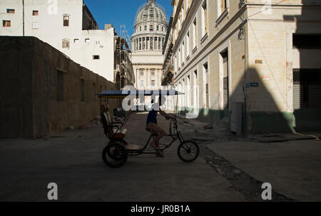 Ein drei Rädern Fahrrad Taxi Paddel im Schatten vorbei an verfallenen Gebäuden und der Hauptstadt Nacional Gebäude in Havanna Kuba Stockfoto