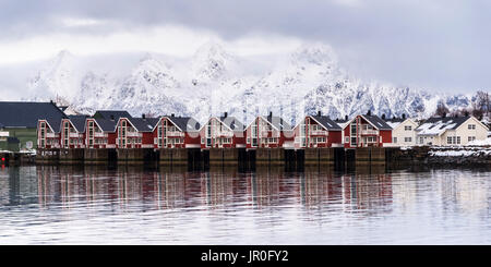 Rote Gebäude entlang des Wassers mit Schneebedeckten Bergen im Hintergrund; Svolvar, Lofoten, Nordland, Norwegen Stockfoto