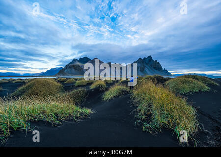 Person, die auf einem schwarzen Sand Damm Betrachten oder Vestrahorn Stokknes an der südlichen Küste von Island; Höfn, Island Stockfoto