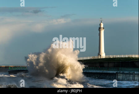 Eine große Welle Krachen gegen die Wand an der Küste unten ein Leuchtturm; Sunderland, Tyne und Wear, England Stockfoto