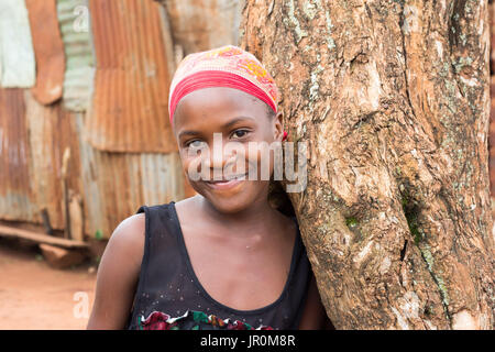 Einen schönen schwarzen afrikanischen Jungen Mädchen lächelnd und lehnte sich gegen einen Baum Stockfoto