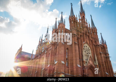 Sunburst auf der Außenfassade mit seinen Rundbogenfenstern aus einer alten roten Ziegeln katholische Kirche vor einem bewölkten blauen Himmel in eine spirituelle, religiöse Hinterg Stockfoto