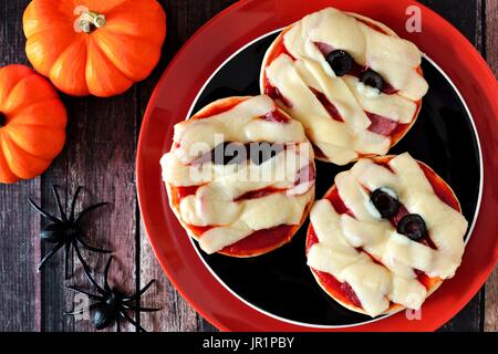 Halloween Mumie Minipizzas auf schwarz und orange Platte über rustikale Holz Hintergrund Stockfoto