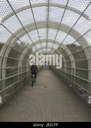 Mädchen in schwarz Fahrradtouren in einen Tunnel über eine Autobahn in Brooklyn New York. Alternative Verkehrsmittel, Autos, Reiten eine Fahrradstadt an einem trüben Tag im Stockfoto